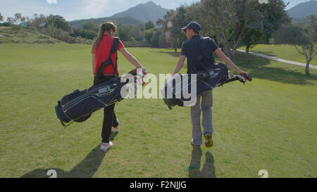 Caucasian couple transportant des sacs de golf on course Banque D'Images