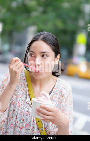 Hispanic woman eating le yogourt glacé sur les trottoirs de la ville Banque D'Images