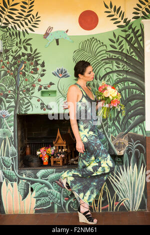 Woman wearing dress matching wallpaper Banque D'Images