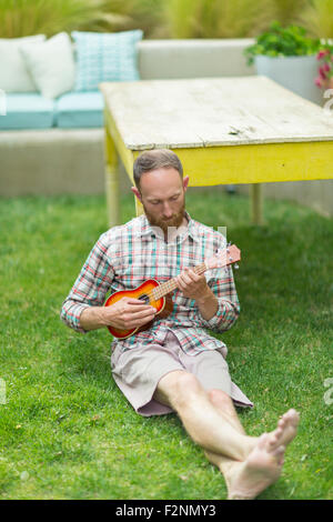 Young man playing ukulele in backyard Banque D'Images