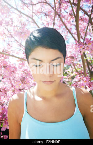 Hispanic woman standing en vertu de l'arbre en fleurs Banque D'Images