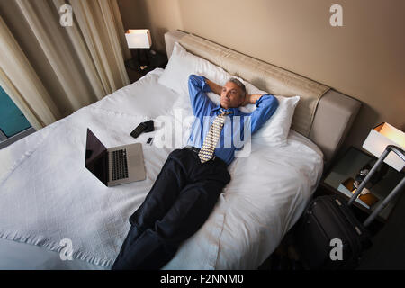 Caucasian businessman fixant avec laptop on hotel bed Banque D'Images