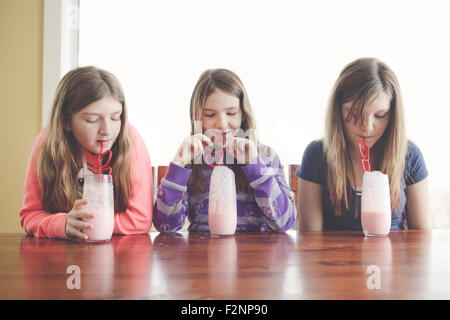 Filles caucasiennes boire du lait avec une paille enroulée à table Banque D'Images