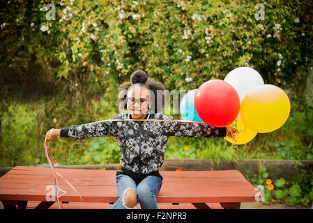 Black girl holding bunch of balloons sur table de pique-nique Banque D'Images