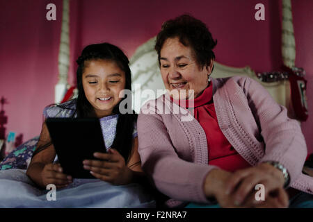 Grand-mère et petite-fille hispanique using digital tablet on bed Banque D'Images