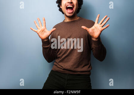 Un jeune homme excité contient jusqu'ses mains jazz, souriant d'ouvrir grand la bouche. Banque D'Images