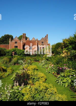 Chenies Manoir et jardin en contrebas avec de belles fleurs vivaces à feuillage vert frais et ensoleillé;avec ciel bleu. Banque D'Images