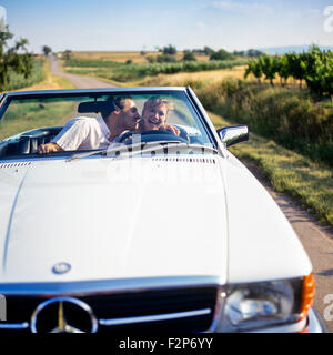 Homme embrassant une femme pilote en conduisant une Mercedes décapotable sur route de campagne, Alsace, France, Europe Banque D'Images