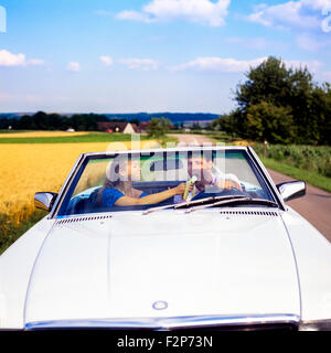 L'alimentation de la femme pilote avec une banane en conduisant une voiture décapotable Mercedes on country road, Alsace, France, Europe Banque D'Images