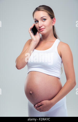 Portrait d'une belle femme enceinte, parler au téléphone et à la caméra à isolé sur fond blanc Banque D'Images