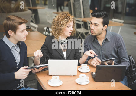 Les gens d'affaires multiraciale travailler assis dans un bar avec des dispositifs technologiques comme comprimé et ordinateur portable. Elle indique pour eux quelque chose à l'écran - la technologie, l'emploi, concept multitâche Banque D'Images