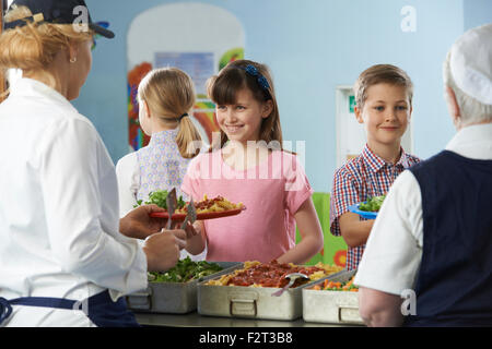 Les élèves d'être servi avec dîner santé en cantine scolaire Banque D'Images