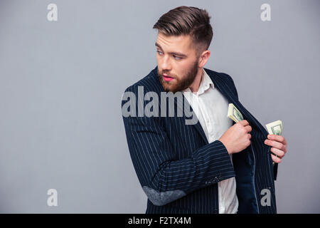 Portrait of a businessman mettant l'argent dans la veste et à l'écart sur fond gris Banque D'Images