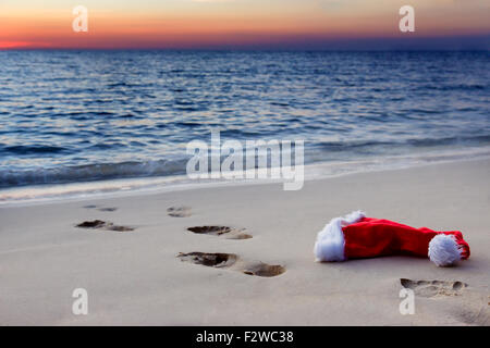 Les empreintes de pas sur une plage de sable fin avec Santa Claus hat au coucher du soleil Banque D'Images