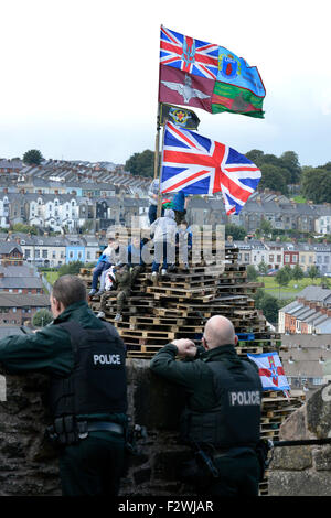 Les agents de l'observation de jeunes nationalistes PSNI debout sur un grand feu fait à partir de palettes en bois, dans le Bogside, Londonderry, N Banque D'Images