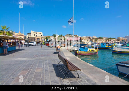 Le restaurant Pier Marsaxlokk avec parasols, bateaux colorés et des signes sur une journée ensoleillée, à Malte. Banque D'Images