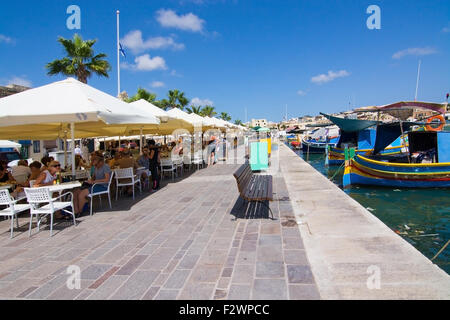 Le restaurant Pier Marsaxlokk avec parasols, bateaux colorés et des signes sur une journée ensoleillée, à Malte. Banque D'Images