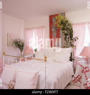 Oreillers garnis de dentelle blanche et couvercle sur laiton lit dans chambre avec 90 rideaux voile rose sur windows Banque D'Images