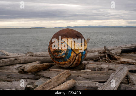 Fer colorés bouée d'échouer sur une plage isolée, jonchée de billes de bois flotté, Garry Point, Steveston, Richmond, BC, Canada Banque D'Images