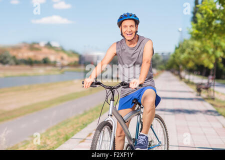 Cheerful senior man in sportswear posant avec son vélo sur un trottoir et regardant la caméra Banque D'Images