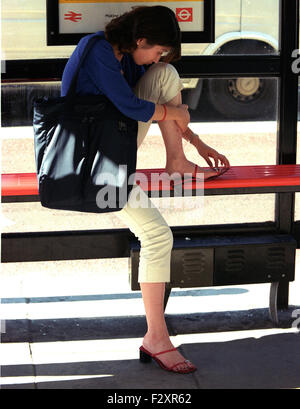 Femme repose à l'arrêt de bus avec des pieds endoloris pour ajuster ses chaussures sortir shopping (crédit de droit©Jack Ludlam) Banque D'Images