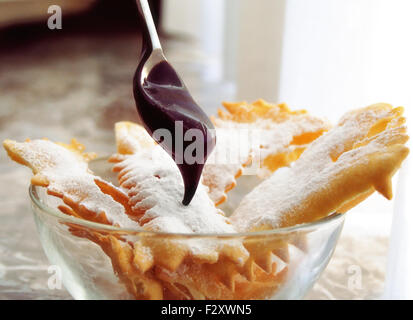 Frappe - beignets de carnaval italien typique saupoudrés de sucre en poudre, avec une cuillère pleine de chocolat fondu. Banque D'Images