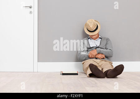 Hauts de dormir sur le plancher avec son chapeau couvrant son visage et appuyé contre un mur à côté d'une porte blanche Banque D'Images