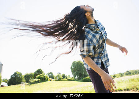 Un jeune homme laisser tomber ses très longs cheveux noirs et de secouer la tête de ventilateur il à l'air frais. Banque D'Images