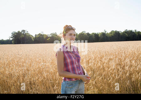 Jeune femme portant une chemise à carreaux debout dans un champ de maïs. Banque D'Images