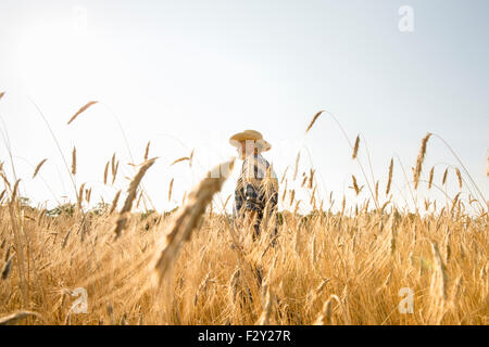 Homme portant une chemise à carreaux et un chapeau debout dans un champ de maïs, un agriculteur. Banque D'Images