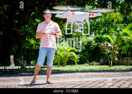 Man avec la commande à distance pour l'exploitation d'un drone quadcopter planant dans l'air. Banque D'Images