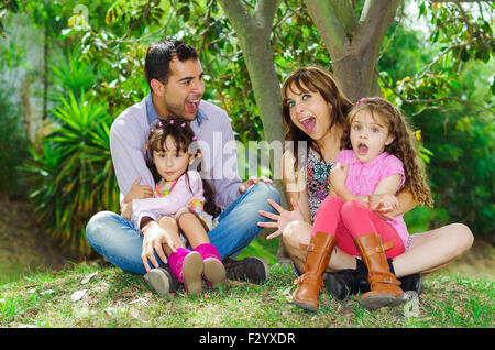 Belle hispanique famille de quatre assis dehors sur l'herbe s'engager dans des conversations tout en se posant naturellement et heureusement Banque D'Images