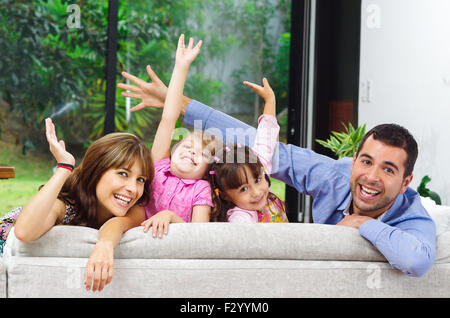 Belle hispanique famille de quatre personnes qui posent avec les chefs qui le retour du canapé à la caméra en souriant Banque D'Images