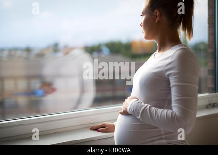 Une femme enceinte en regardant par la fenêtre Banque D'Images