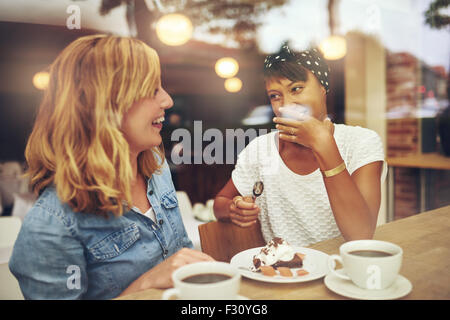 Deux bonnes amies, savourer une tasse de café ensemble dans un café avec un rire que l'autre fait un geste d'em Banque D'Images