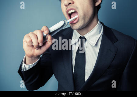 Jeune homme d'affaires est le brossage des dents avec une brosse à dents électrique Banque D'Images