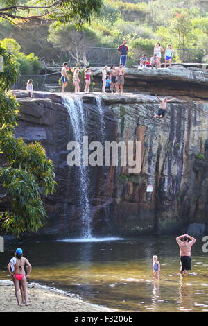 Une foule regarde comme un homme dans la vingtaine saute la falaise dans un trou de natation à Wattamolla, près de Sydney, Australie. Banque D'Images