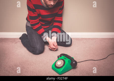 Un jeune homme est assis sur le plancher et est désespérément en attente d'un appel téléphonique Banque D'Images