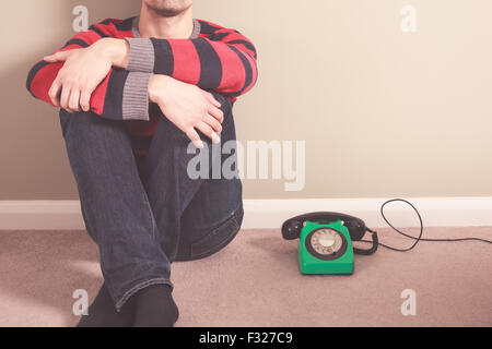 Jeune homme est assis sur le plancher avec un vieux téléphone à cadran Banque D'Images