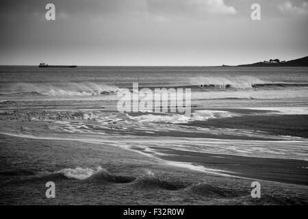 Un porte-conteneurs passe par ondes ensoleillées que Pentewan sands approche, Cornwall. Paysage en noir et blanc. Banque D'Images