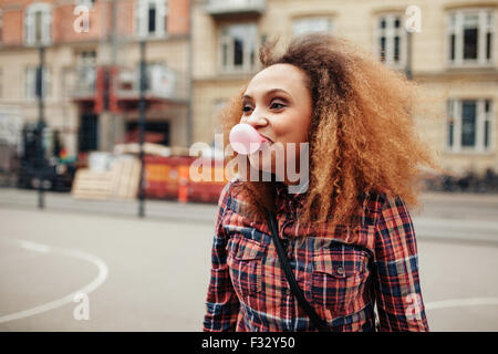 Jeune femme africaine souffle une bulle avec son chewing-gum. Casual young woman on city street s'amusant. Banque D'Images