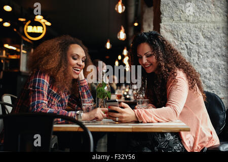 Les jeunes femmes assis à un café et à l'aide de téléphone. Amis assis dans un restaurant avec une femme montrant quelque chose d'intéressant à son Banque D'Images