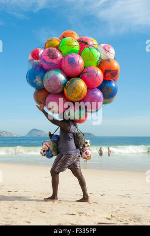 RIO DE JANEIRO, Brésil - le 20 janvier 2013 : : Plage vendeur vente de ballons de plage coloré porte ses marchandises le long de la plage d'Ipanema Banque D'Images