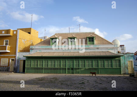 Grande maison en bois orné, avec longue rangée de volets verts et un chien devant à Boa Vista sur l'île république du Cap-Vert Banque D'Images