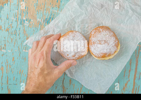 Main mâle atteint et picking sweet donut sucré à partir de la table de cuisine en bois rustique, de savoureux beignets boulangerie overhead shot Banque D'Images