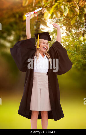 Image composite de l'étudiant diplômé en robe blonde holding up son diplôme Banque D'Images