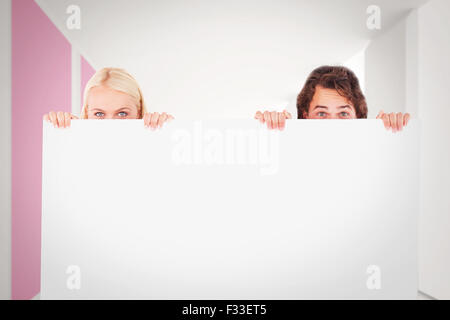 Image composite de l'heureux couple se cacher derrière un tableau blanc Banque D'Images
