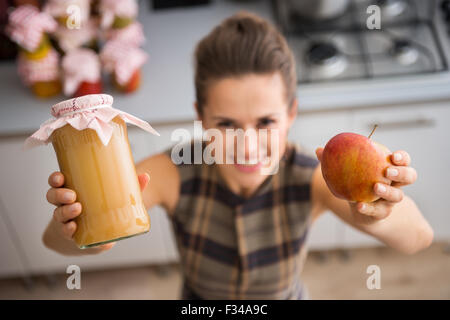 Oh, le goût sucré de la compote de pomme... Une femme heureuse est exhibant son home-made de la compote de pomme, tenant un pot de verre de sauce aux pommes et une pomme fraîche. Banque D'Images