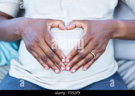 Mid section of woman making heart shape sur son ventre Banque D'Images