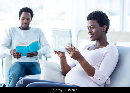 Smiling woman looking at tablet avec man reading book Banque D'Images